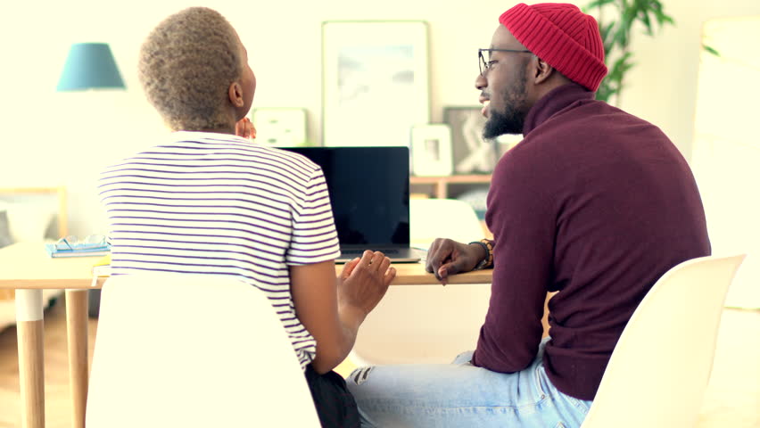 Young African American hipster girl explaining idea to her partner while discussing strategy for cooperation, skilled dark skinned man communicating with female colleague sitting near laptop, a Business & Finance Video by GaudiLab