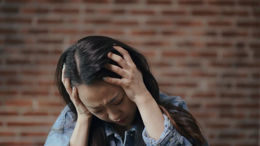 Portrait of beautiful young asian girl holding her head with her hands. Strong tension from the hustle and bustle. Overabundance of information | Shutterstock HD Video #1014333083