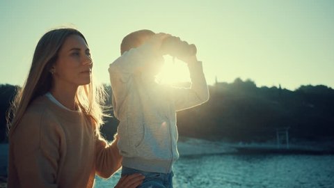Happy Mother and son looking through binoculars on summer day at sunset on a sea background - Βίντεο στοκ