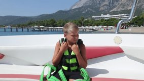 Brave kid sitting in motorboat ready for parasailing flight over summer beach. Family has fun during vacation. Real time full hd video footage.