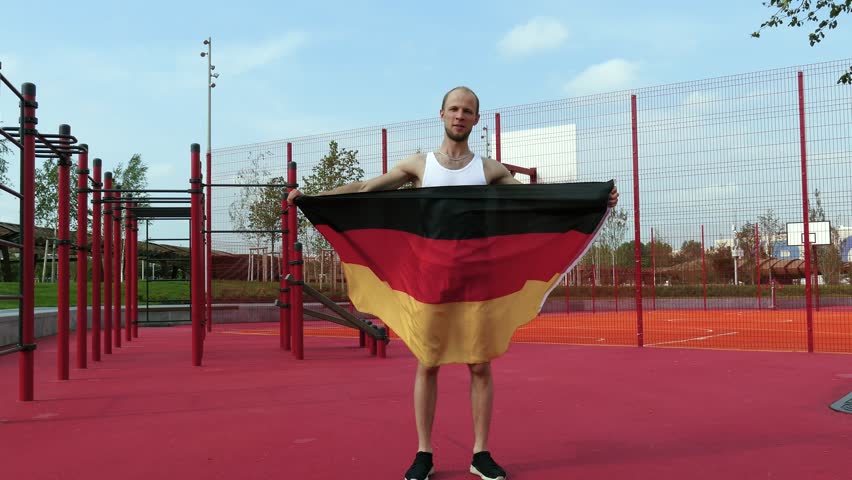 Young Man Holding German National Flag To The Sky With Two Hands