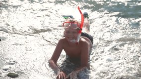 Portrait of happy child wearing mask for snorkelling laying on beach in sea water on sunny sunrise morning. Real time full hd video footage.