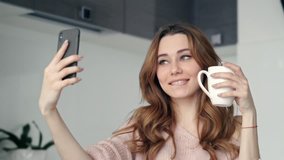 Beautiful brunette woman grimacing and smiling while making selfie with  smartphone in kitchen at home 