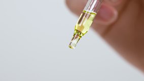Close-up of lavender oil drops are falling from the pipette. The pipette is inclined. On the white background.