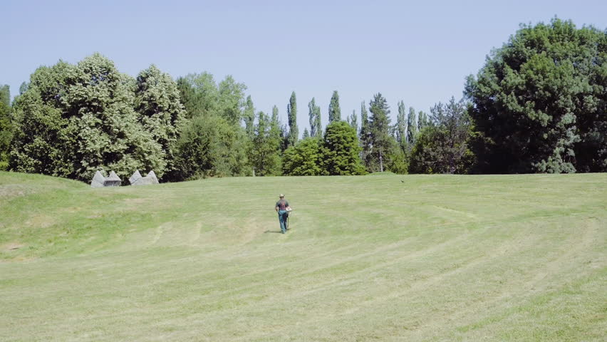 Drone shot above workers while mowing grass with gasoline lawn trimmers in park. Drone shot above greenery male workers mowing weed on area of field with lawn mower.