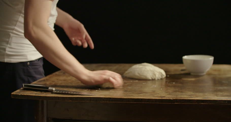 Caucasian man making pizza dough ball on a dark wood table
