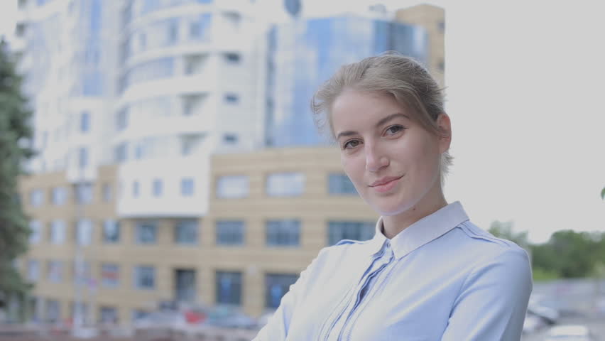 Pretty woman in blouse standing on the buildings background and looking at camera. The girl looks happy. She smiling and posing.