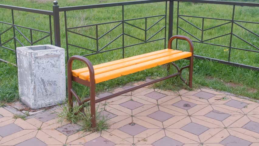 Bench by the fence in park. Near the trash.