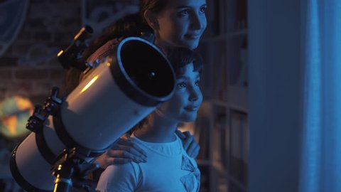 Happy young girls stargazing with a telescope, they are learning astronomy together at home