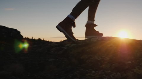 Legs in trekking boots go along the mountain ridge against the backdrop of the rising sun. Travel and adventure concept