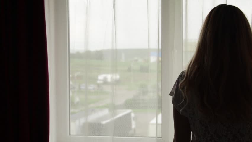 Woman in silhouette dressing a jacket for a weading or event in front of bright window