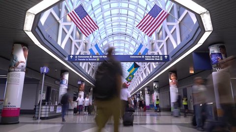 Chicago, Illinois / USA - July 26 2018: 4K 15 second long exposure time lapse of travelers rushing through Chicago O'Hare International Airport hallway with flags of various countries hanging.
