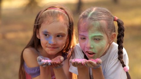 Two girls blow off colored powder from their hands. Holi Festival