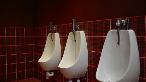 adult man is approaching to urinal in a toilet of restaurant, unfastening pants and peeing