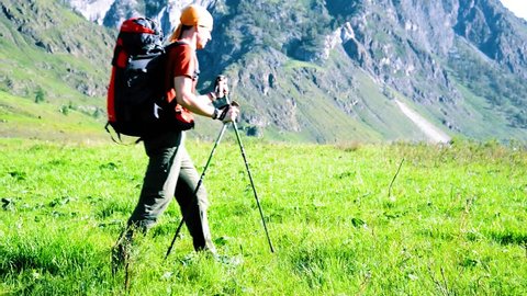 FHD Hiking man walking on green mountain meadow with backpack. Tourist travelling in sunny outdoors. Summer sport and recreation concept.