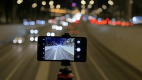 The smartphone is mounted on a tripod. They shoot on video, traffic of cars, against a background of beautiful lights. In evening time.