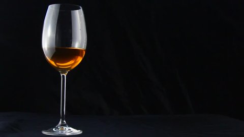 Isolated glass with wine on a black background. White alcohol with white smoke in a beautiful elegant glass cup with a long thin leg. smoking