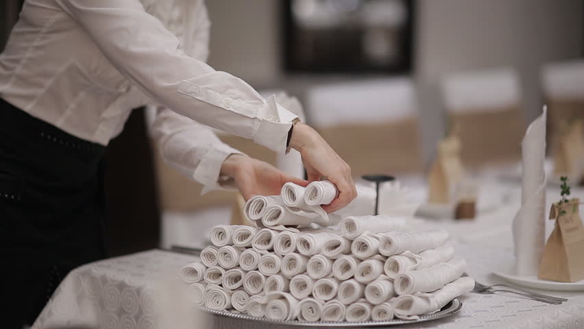 Waiter setting the table in the Banquet hall. The waitress puts the napkins at each plate.