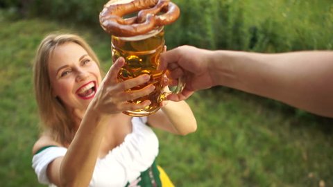 A girl in a traditional Bavarian dress buys beer and pretzel at the Oktoberfest beer festival. A woman laughs cheerfully and enjoys buying. On a green background