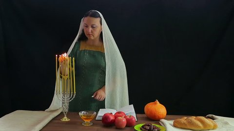 A Jewish woman lights candles in a festive candlestick in honor of Rosh Hashanah and reads a blessing.