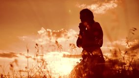 Girl folded her hands in prayer silhouette at sunset. woman praying on her knees. slow motion video. Girl folded her hands in prayer pray to God. the girl praying asks forgiveness for lifestyle sins