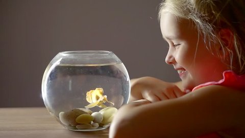 Baby girl, watching and playing for the goldfish, who lives in a home round aquarium with water