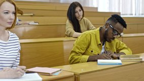 Medium shot of cute blonde girl sitting at desk with multi ethnic groupmates and taking notes during lecture at university - Powered by Shutterstock - Get 15% off with code: PIKWIZARD15