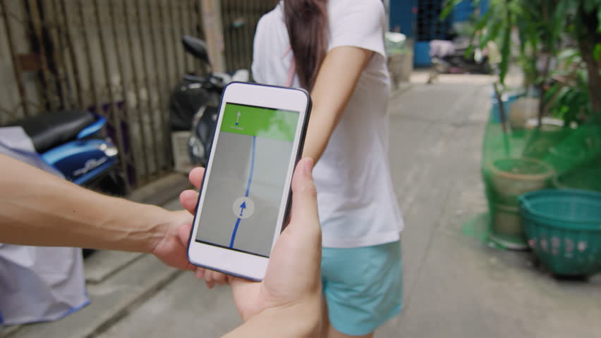 Asian couple walking together looking for an address with a gps navigator on a smartphone in Bangkok city alleyway street in Thailand Asia. Slow motion