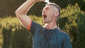 Beautiful fitness athlete man drinking water after work out exercising on sunset evening summer in the park. Video footage in Full HD video (1920x1080). Slow motion in 100/25fps