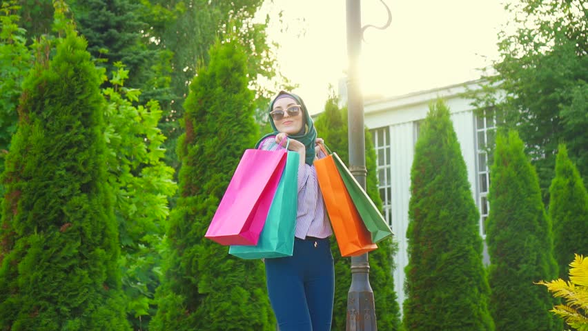 Young muslim woman in hijab circling with bags in her hands after shopping.