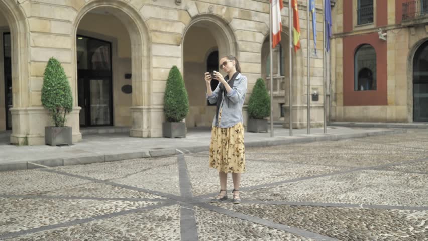 4 k beautiful young girl in jeans jacket, yellow broad skirt typing mobile phone at the old european street