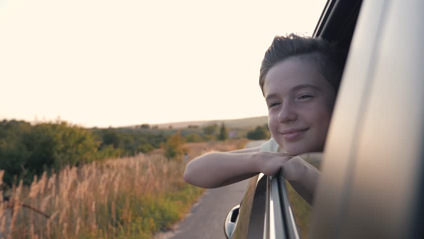 Teen boy looking out car window. Summer trip with family. Boy is dream. Happy boy traveling with family. Dream kid. Happy family traveling by car. Smile of kid in car window | Shutterstock HD Video #1014476459