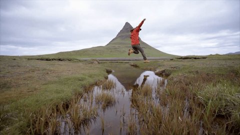 Man hiking in Iceland jumps a small creek.
Slow motion shot of a young man on a hike in Iceland jumping over a small creek, mountains in the background 