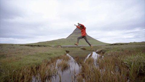 Man hiking in Iceland jumps a small creek. Slow motion shot of a young man on a hike in Iceland jumping over a small creek, mountains in the background 