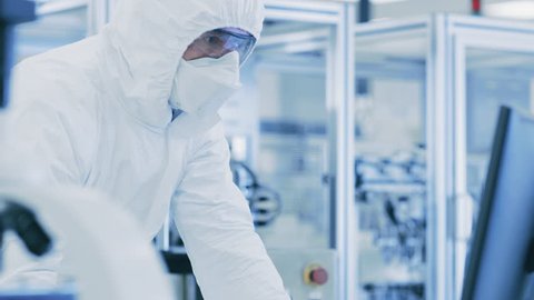 In Laboratory Scientists in Protective Clothes Doing Research, Using Microscope and Entering Data into Personal Computer. Modern Manufactory Producing Semiconductors. Shot on RED EPIC-W 8K Camera.