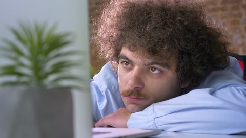 Sleepy funny businessman with curly hair dozing at work, sleeping at workplace in modern office