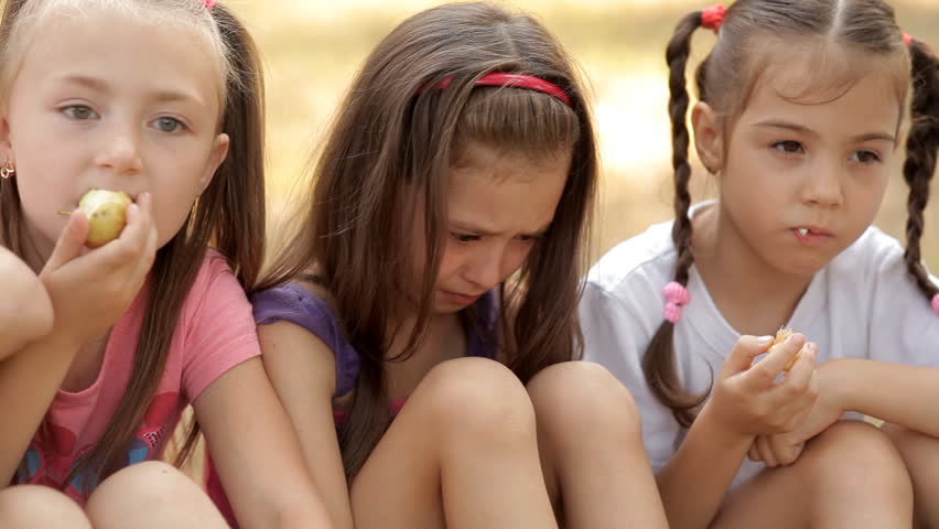 Children spend time on the lawn in the park, eat apples. One child was upset and offended