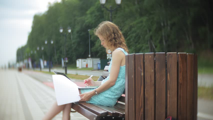 A woman sitting on a bench on the beach enjoys a laptop in a reading document 4k