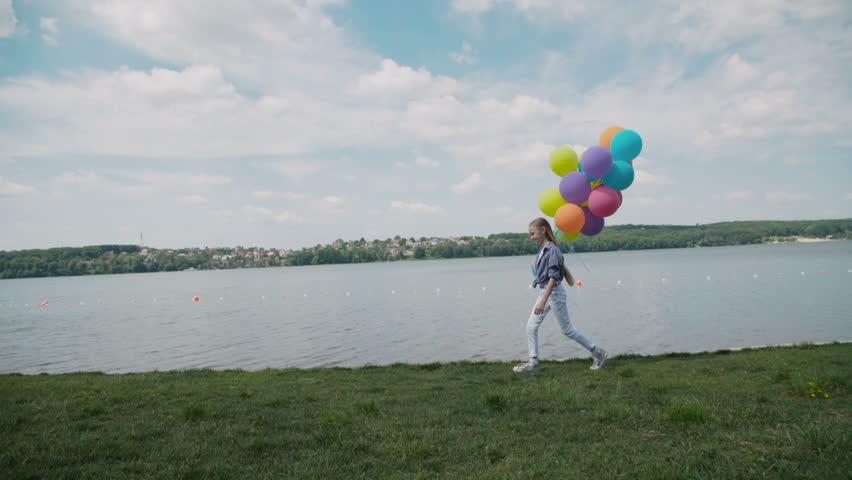 Pretty young girl runs with balloons in hand at coustline. 4K.