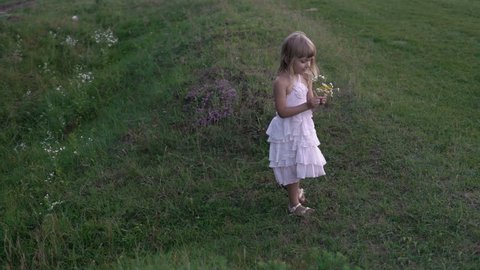 little girl in a white dress playing with flowers on the green field