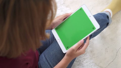 Young asian woman using black tablet device with green screen. Asian woman holding tablet, scrolling pages while sitting on the couch in the living room. Chroma key.