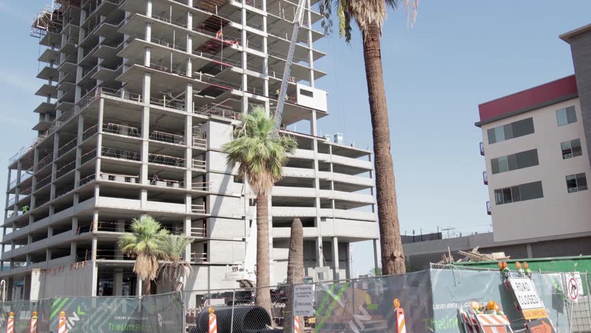 4k vertical panning shot of a large tower under construction in Phoenix, Arizona with foregroud/background interest.  Workers can be seen in the distance and ambient construction noise is present.