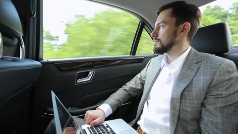 Businessman with laptop in back seat of car looking thoughtfully out window