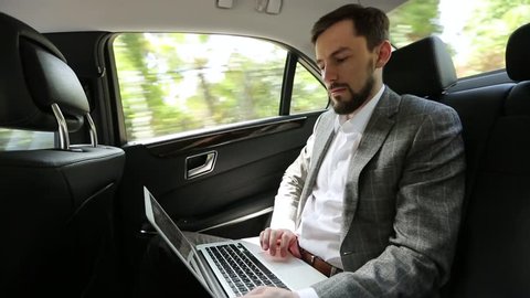 Businessman in suit travels with laptop in the back seat of the car