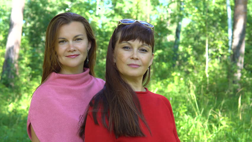 Sisters. Portrait of two smiling women dressed in pink and red sweater. In the background a blurred forest.