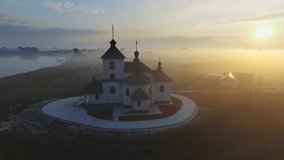 Aerial footage video of small village church at the foggy morning. Sunrise time. Kyiv region, Ukraine. Flying over the Desna river