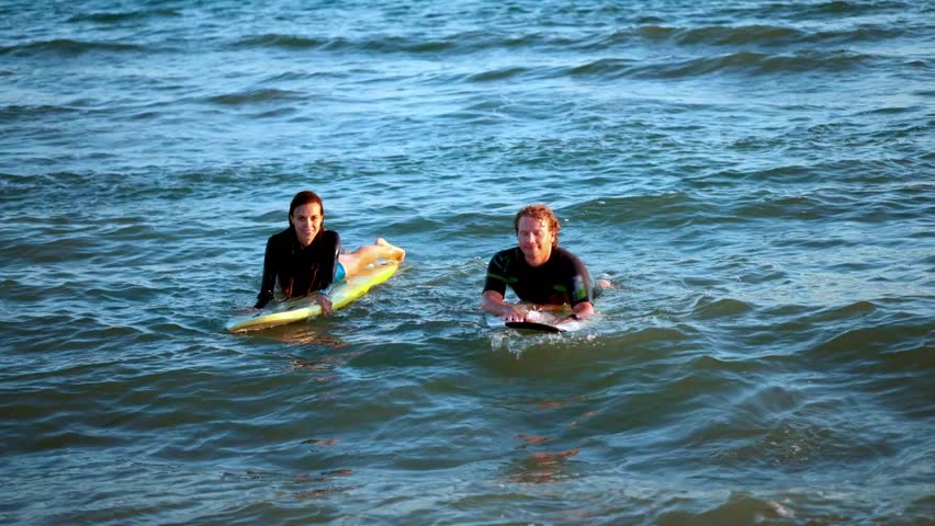 two surfers swim on surfboards in the open sea, waiting for the wave.