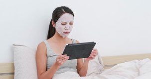 Woman apply facial mask and watching on tablet at home