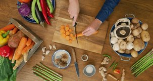 Overhead view of woman's hands cutting carrot. Female is slicing fresh orange vegetable on cutting board. Various nutritious food in kitchen at home. Shot on RED Camera.