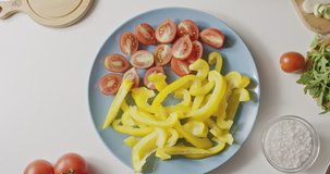 Circular movement counter-clockwise in 4K. Top view on natural organic ingredients, vegetables for salad. Sliced ripe red tomatoes and yellow paprika on a blue ceramic plate on a white kitchen table.